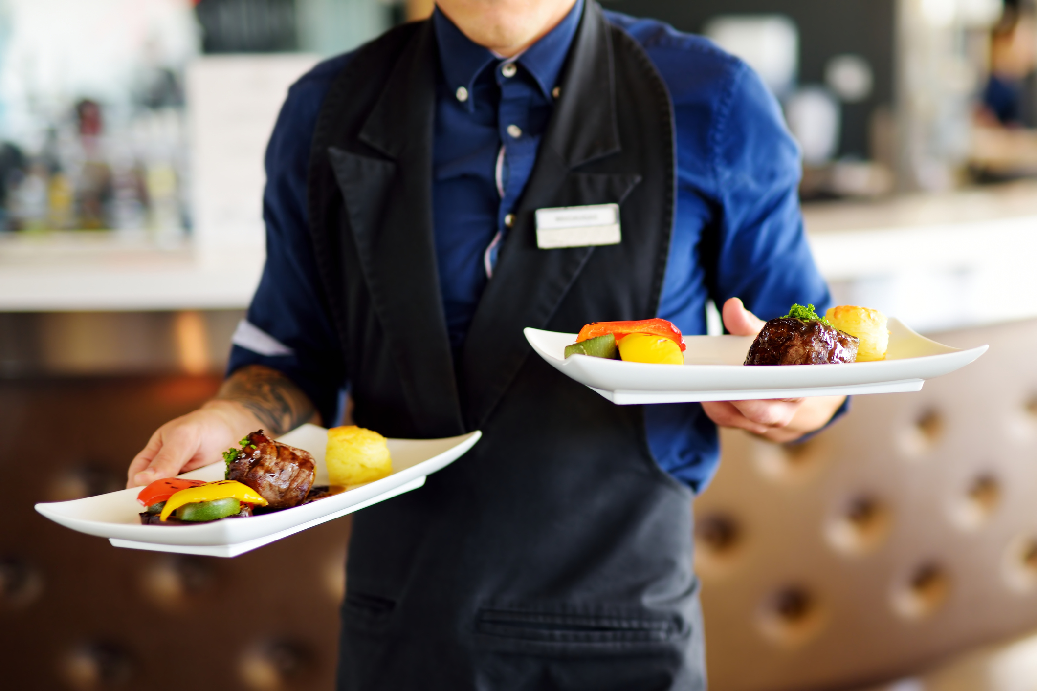 Waiter carrying two plates with meat dish on some festive event ServSafe Food Handler Training