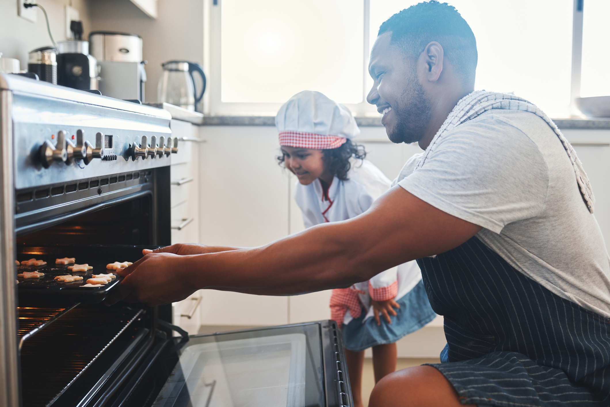 Shot of a man and his daughter putting a baking tray in the oven Shot of a man and his daughter putting a baking tray in the oven